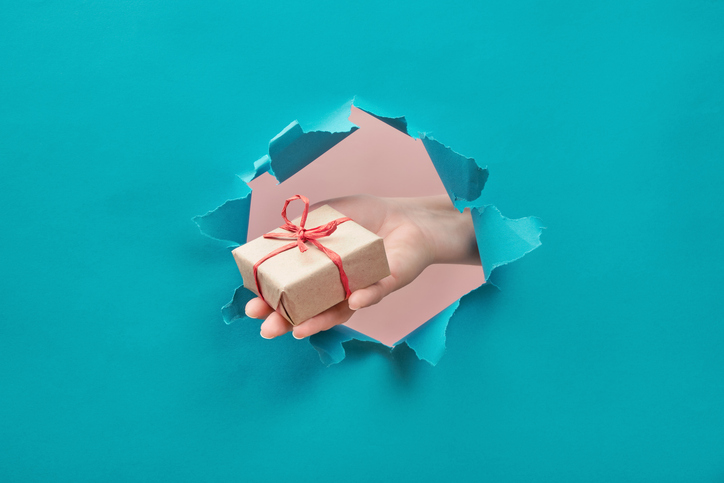 Hand holding a wrapped gift through torn paper, symbolizing free gifts included in charity fundraising appeals.