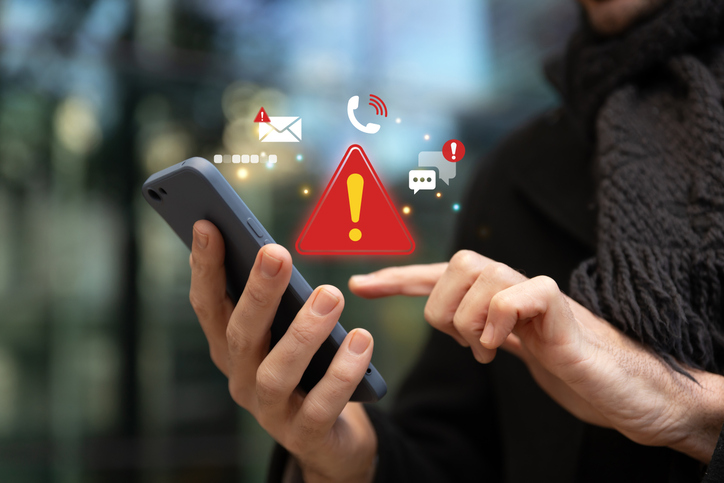 Man using a smartphone with red warning icons representing online charity impersonation scams and fake donation alerts.