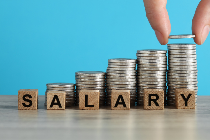 Woman placing coins beside wooden blocks spelling salary, illustrating charity compensation.