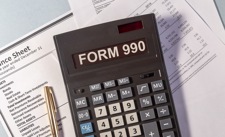 Calculator displaying Form 990 beside financial papers and a pen