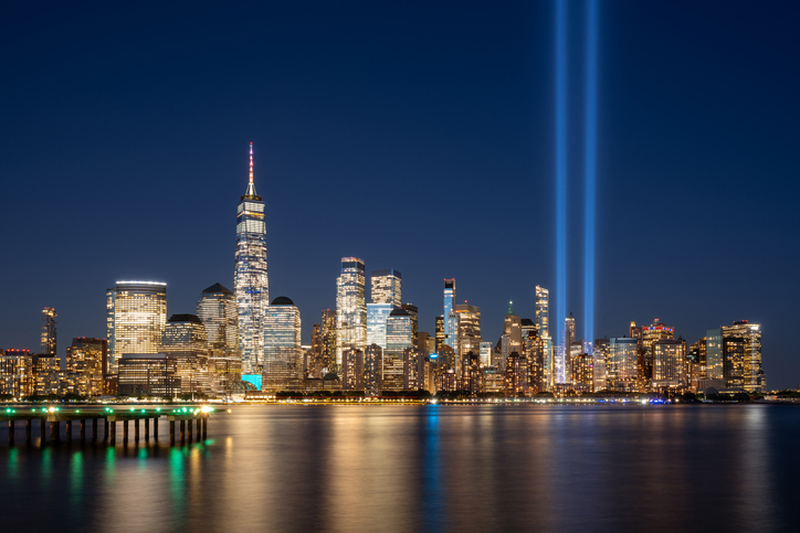 September 11 Tribute in Light shining above the Lower Manhattan skyline at night, with the Hudson River in the foreground.